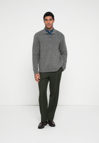 Grauer Strickpullover mit Kragen und drei Knöpfen, kombiniert mit dunkelgrüner Hose und braunen Schuhen. Einfaches, strukturiertes Design.