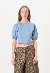 Ljusblå cropped topp med puffärmar och rundad halsringning, kombinerad med leopardmönstrade höga byxor. Slät denimmaterial.