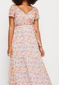 Abito a trapezio floreale con maniche a palloncino corte. Tessuto leggero e trasparente con una base pastello e motivi floreali arancioni, rosa e viola. Dettaglio della vita legata.