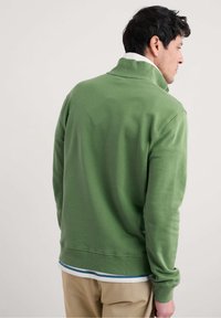 Grüner Sweatshirt mit hohem Kragen, langen Ärmeln und gerippten Bündchen. Der Stoff wirkt weich, hat eine schlichte Textur und einen geschichteten Saum.