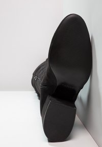 Bota de ante negra hasta el tobillo con suela de goma y cremallera lateral, con una forma contorneada y suela texturizada para mayor agarre.