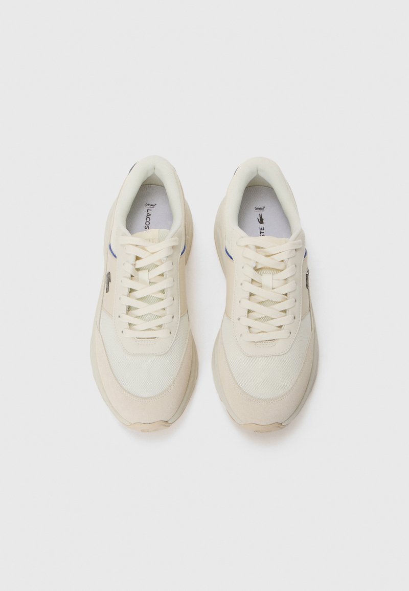 Une paire de baskets Lacoste blanc cassé avec des accents en suède beige, des panneaux en maille et des lacets crème sur un fond blanc.