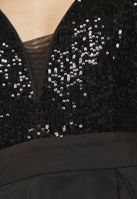 Corsage de robe noir avec des sequins noirs brillants et un panneau en mesh noir transparent au décolleté plongeant en V.