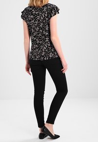 Svart blommig blus med korta volangärmar, matchad med svarta skinny jeans. Blusen har ett litet rosa blommönster. Svarta platta skor.