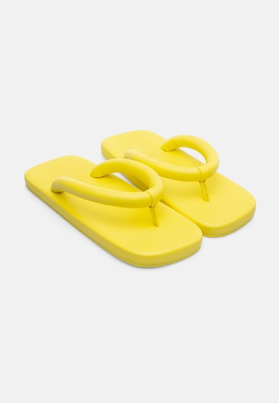 Tongs jaunes avec une semelle plate et lisse, des brides rondes et un design minimaliste. Fabriquées en matériau durable et flexible.