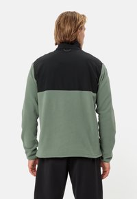 Giacca in pile verde con pannello superiore nero, colletto alto e maniche lunghe. Presenta una texture liscia e un design pulito senza decorazioni.