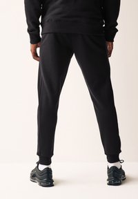 Sorte sweatpants med tapered fit og ribbede manchetter, lavet af blødt stof, båret med sorte sneakers og hvide sokker. Minimalistisk design.