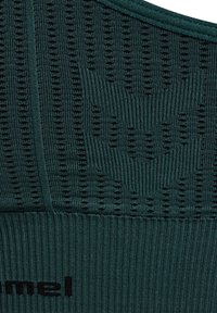 Ciemnozielona dziana tkanina z teksturowanym wzorem, zawierająca prążkowane sekcje oraz czarne logo. Gładki, elastyczny materiał o dopasowanym kroju.