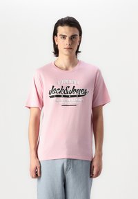 Rožinė medvilnės marškinėliai su juodu grafiniu spaudiniu, kuriame matyti tekstas "Jack & Jones" ir "Fine Cotton Garments". Apykaklė suapvalinta ir trumpomis rankovėmis.