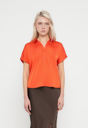 Kortermet, v-halset bluse i lyst oransje satin, med knappestolpe foran og løs passform, kombinert med et brunt skjørt.