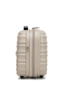 Valigia rigida di un beige chiaro, con un design a righe testurizzate, zip argentata e quattro ruote nere per la mobilità.