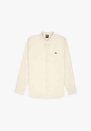 Beige overhemd met lange mouwen, knopen en kraag, met klein zwart logo op het linkerborstzakgebied, plat gelegd op een witte achtergrond.