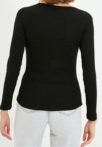 Svart långärmad topp i ribbat material. Har en rund halsringning och en figurnära passform. Bärs med ljusa jeans.