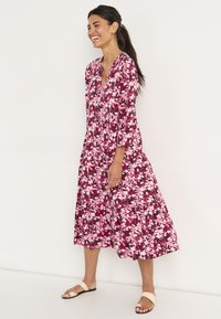 Bloemenjurk met een diepe V-hals, lange mouwen, een gelaagde rok en een roze en paarse kleurenschema met een gedurfde bloemenprint.
