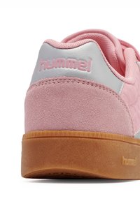 Różowy zamszowy sneaker z srebrnym akcentem, posiadający teksturowane panele i gumową podeszwę. Logo widoczne z tyłu.