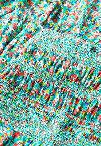 Kolorowa tkanina w kwiaty, głównie turkusowa z czerwonymi i żółtymi akcentami. Posiada marszczoną teksturę oraz detale smockingu w różnych sekcjach.