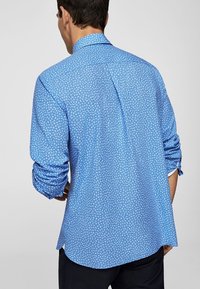Camicia blu a maniche lunghe con un piccolo motivo floreale bianco, dotata di colletto standard e maniche arrotolate, realizzata in tessuto leggero.
