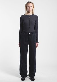 Harmaa ribattu pitkähihaisella puserolla, jossa on napit edessä, yhdistettyinä löysiin mustiin farkkuihin, joissa on tasainen vyötärö ja etutaskut.