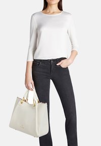 Maglietta bianca a maniche lunghe, jeans neri e una borsa bianca strutturata con dettagli dorati e una finitura testurizzata, tenuta da una mano.