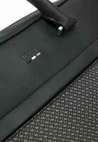 Sort lædertaske med en struktureret nederste sektion med et geometrisk mønster. Sølv hardware og præget logo detaljer i tre farver.