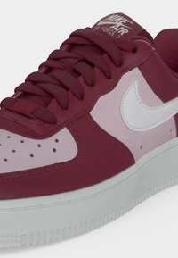 Κοντινό πλάνο ενός αθλητικού παπουτσιού Nike Air Force 1 σε σκούρο κόκκινο και ανοιχτό ροζ με λευκό σήμα και κορδόνια σε σκούρο κόκκινο χρώμα.