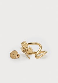 Gold stainless steel earrings featuring a curved, twisted design and a circular stud with a logo. Smooth texture, minimalist style.