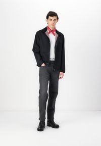 Black jacket with a collar, red bandana, white shirt, gray jeans, and black boots. Notable button details and relaxed fit.