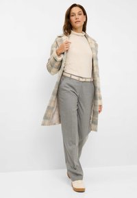 Beige en grijs geblokte jas over een crèmekleurige coltrui, grijze op maat gemaakte broek en lichte sneakers. Zachte texturen met een ontspannen pasvorm.