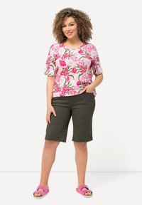 Růžový top s krátkým rukávem a vzorem mušlí, spárovaný s tmavě zelenými šortkami a růžovými sandály. Má uvolněný střih a neformální design.