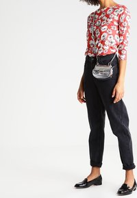 Rode bloemen blouse met lange mouwen, zwarte tapering broek met opgerolde boorden, en glanzende zwarte loafers. Kleine zilveren schoudertas met klepsluiting.