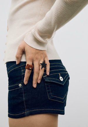 Mørke denim shorts med en figursyet pasform, der har sølvhardware og baglommer. To ringe: en med brun bjørn design, en med sort stjerneform.