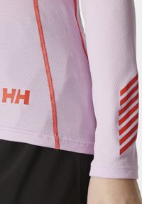 Top de manga larga color rosa claro con tejido texturizado, acentos rojos contrastantes a lo largo de las costuras y patrón a rayas en la manga. Prenda inferior oscura.