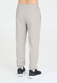 Hellgraue Sweatpants aus weichem Stoff, mit elastischem Bund und Seitentaschen, kombiniert mit schwarzen Sportschuhen.