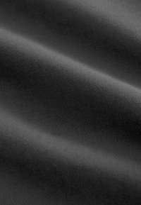 Zachte zwarte stof met subtiele diagonale weefstructuur en zachte plooien die zachte schaduwen creëren.