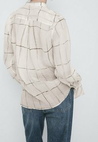 Lyse beige langærmet skjorte med et ternet mønster i mørkebrune linjer; løs pasform og blødt stof; parret med blå denim jeans.