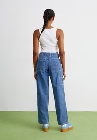 Šviesiai mėlyni denimo krovinių kelnės su plačiomis kojomis, dviem užpakalinėmis kišenėmis ir šoninėmis kišenėmis. Sukomplektuota su šviesiai mėlynais batais ir balta topu.