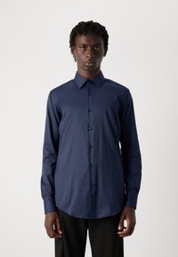 Camisa de manga larga azul marino hecha de tela suave, con cuello tipo solapa, cierre de botones y un corte estructurado con un dobladillo curvado.