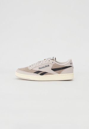 Baskets en suède gris clair avec des accents noirs et une semelle crème. Présentent un design à lacets et une étiquette de langue de marque, offrant une esthétique rétro.