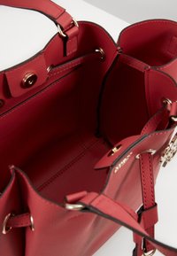 Borsa a tracolla in pelle rossa con esterno testurizzato. L'interno presenta una fodera liscia, cinturini regolabili e dettagli in metallo color oro.