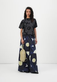 Black floral short-sleeve top paired with wide-leg patterned pants featuring yellow and navy circles. The model holds a drawstring bag.