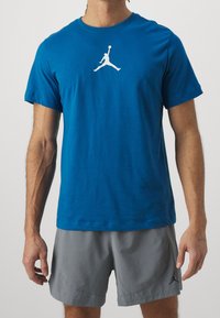 Blå bomullströja med en vit Jordan-logotyp på bröstet, kombinerad med grå shorts, som visar en avslappnad passform och mjuk textur.