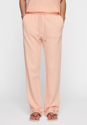 Pantaloni della tuta color pesca realizzati in un tessuto morbido, dotati di una vita elastica con cordoncino, tasche laterali e una vestibilità comoda.