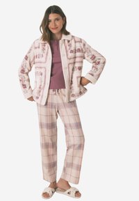 Fleecejacka med blommönster i rosa och vitt, lagd över en rosa topp; matchad med rutiga, vida byxor i mjuka färger.