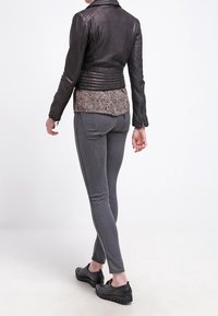 Sort læderjakke med quiltet tekstur, båret over en leopardprint bluse. Grå skinny jeans og sorte slip-on sko fuldender outfittet.