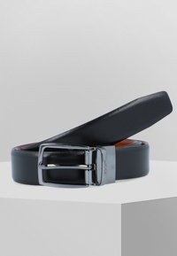 Svart lærbelte med en glat overflade, som har en sølvfarget metallspenne. Den indvendige side er brun, noe som viser et to-farget design.