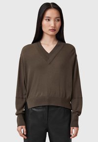 Maglione marrone a V con maniche lunghe, orlo a coste e texture morbida, abbinato a pantaloni di pelle nera, presentato su uno sfondo neutro.