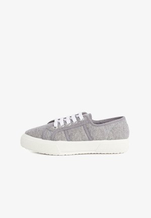 Zapatilla textil gris con cordones blancos, de perfil bajo, suela de goma y detalles texturizados en la punta y paneles laterales.