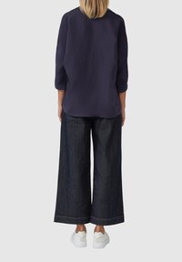 Chemisier bleu marine à manches longues avec une coupe décontractée, associé à un pantalon en denim large et sombre. Des baskets blanches complètent la tenue.
