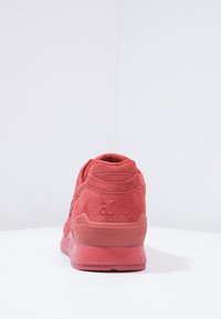 Röd mockaskor med en slät yta, rund häl och vadderad krage. Har präglad logotyp och gummisula för bra grepp.