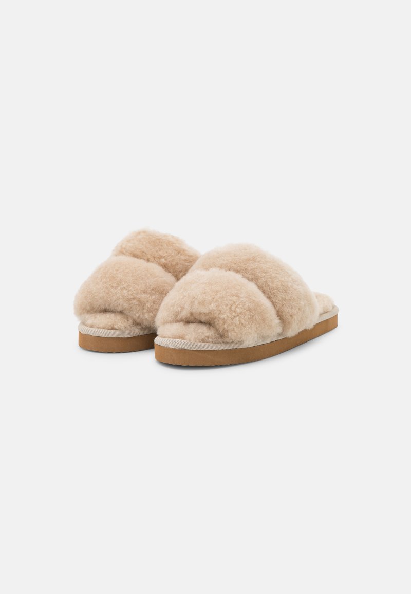 Beige, mit Fell gefütterte Hausschuhe mit einem Kreuzband-Design, weicher Textur und flacher, beigefarbener Sohle. Keine sichtbaren Beschläge oder Muster.